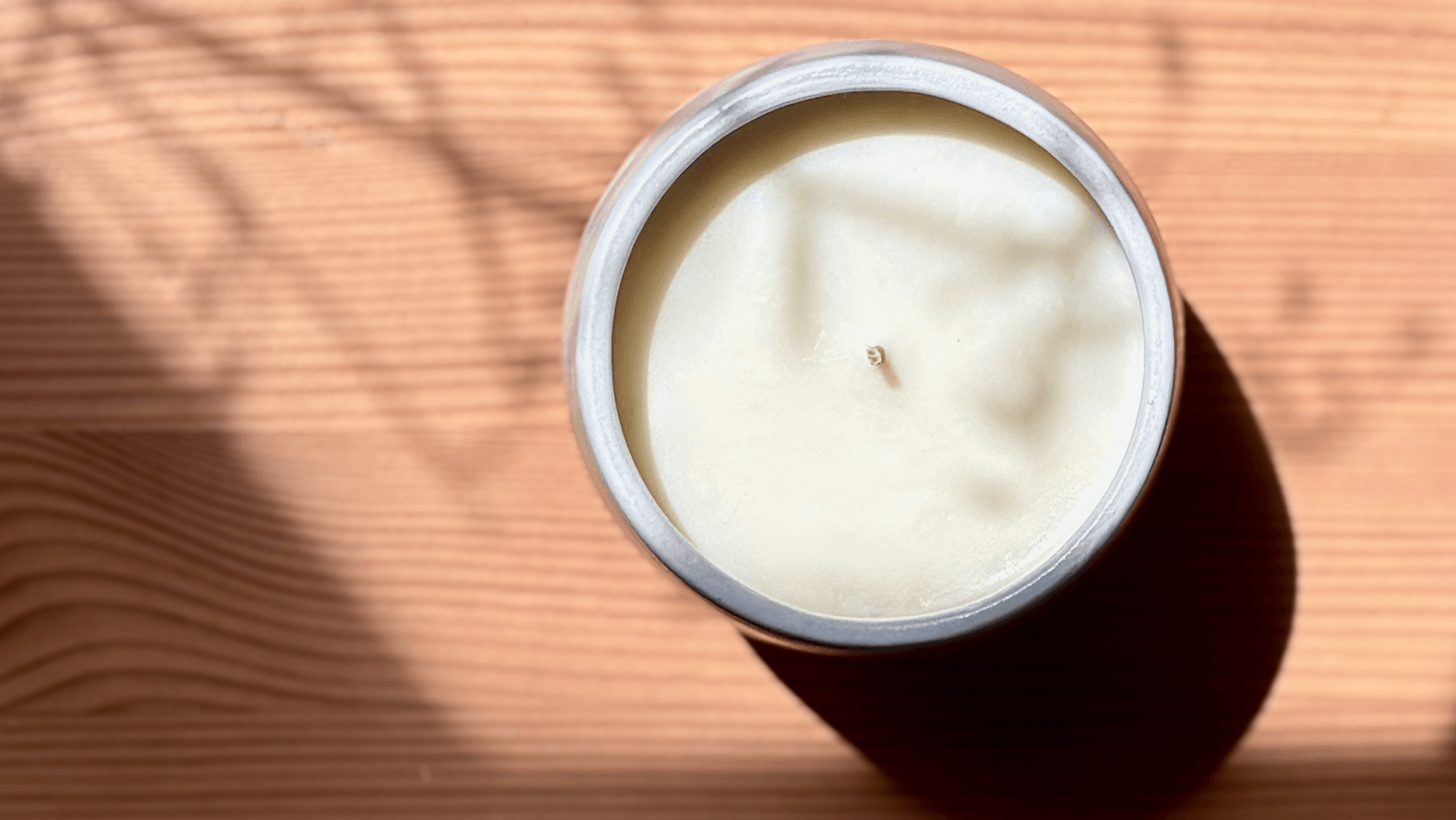 Organic candle in white ceramic vessel on a wooden surface, shown from an aerial perspective.