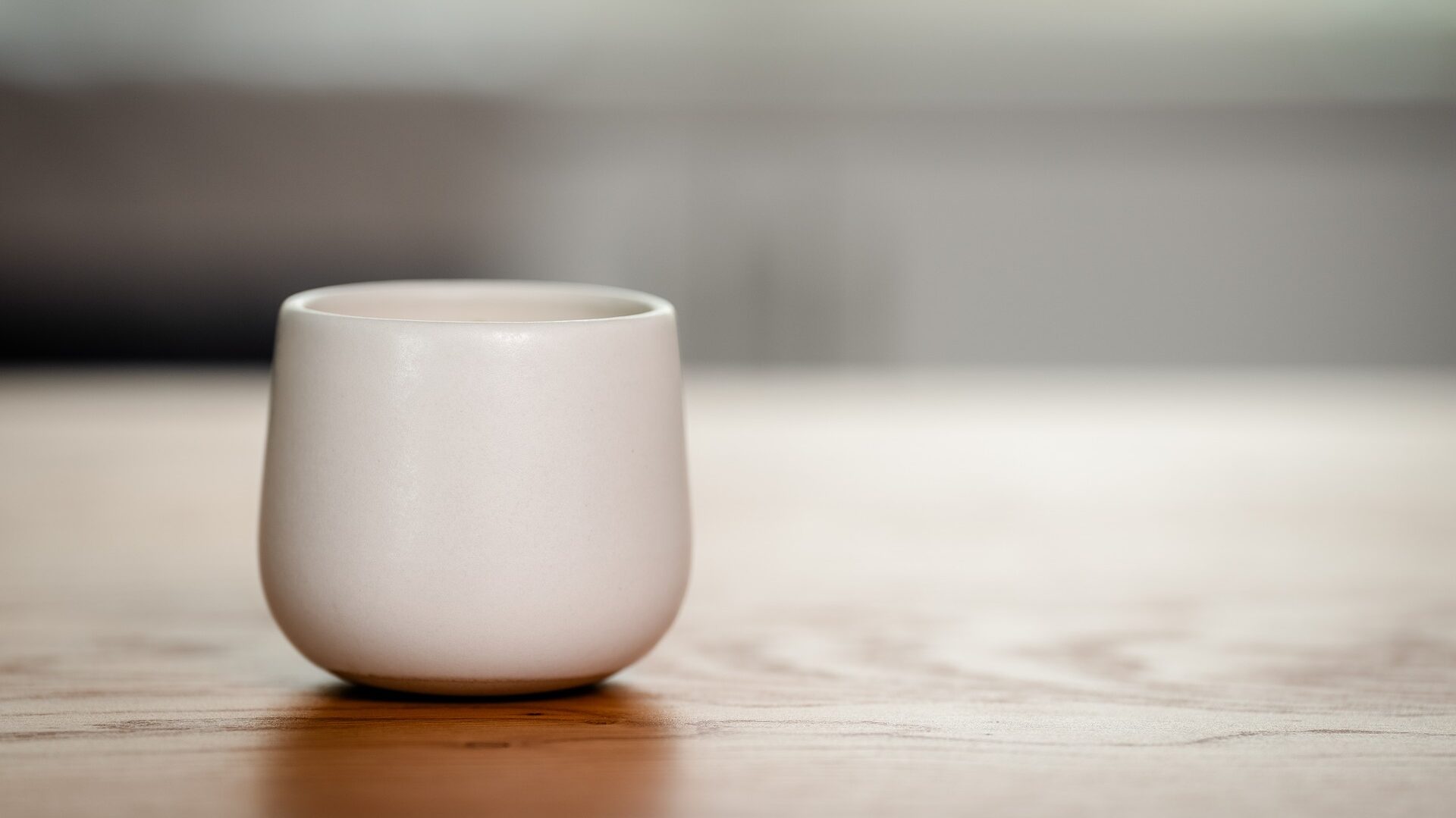 Organic candle in a white ceramic vessel on a wooden surface.