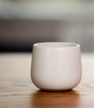 Organic candle in white ceramic vessel on wooden surface.